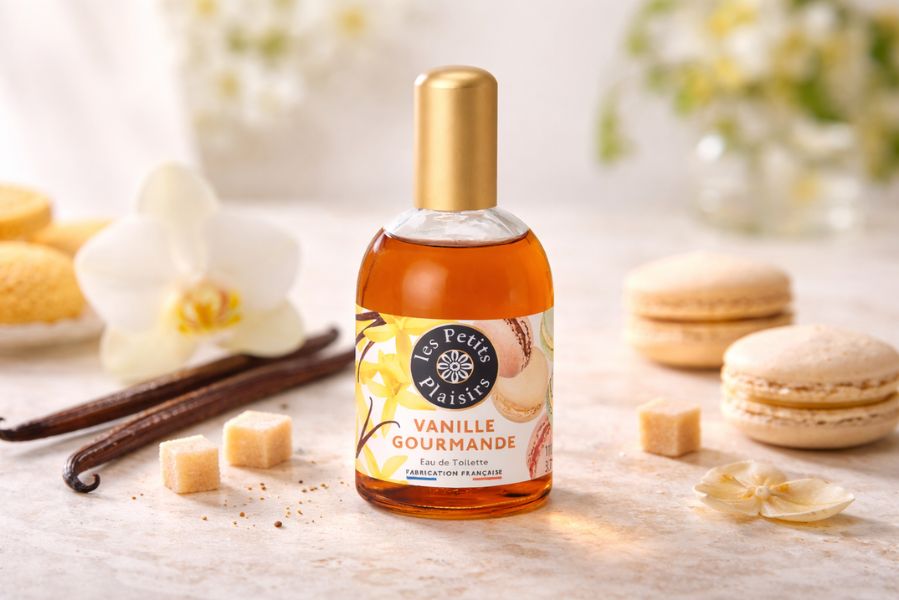Flacon d’eau de toilette Vanille Gourmande Les Petits Plaisirs entouré de gousses de vanille et macarons dans une ambiance douce et lumineuse.